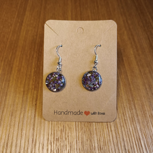 Pair of purple floral earrings on a brown card with 'Handmade with Love' text, placed on a wooden surface.